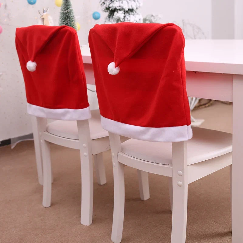 Two Santa hat chair covers on white dining chairs beside a Christmas table