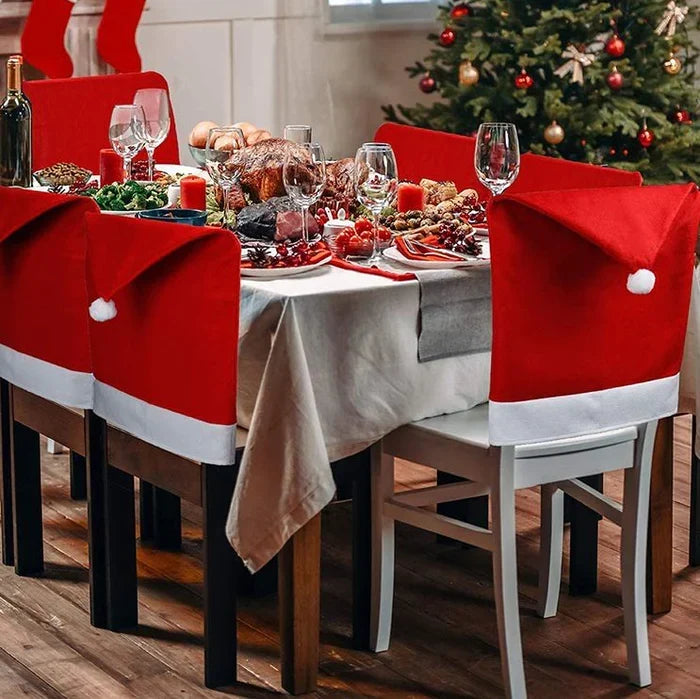 Santa hat Christmas chair covers on dining chairs around a festive table with a Christmas tree